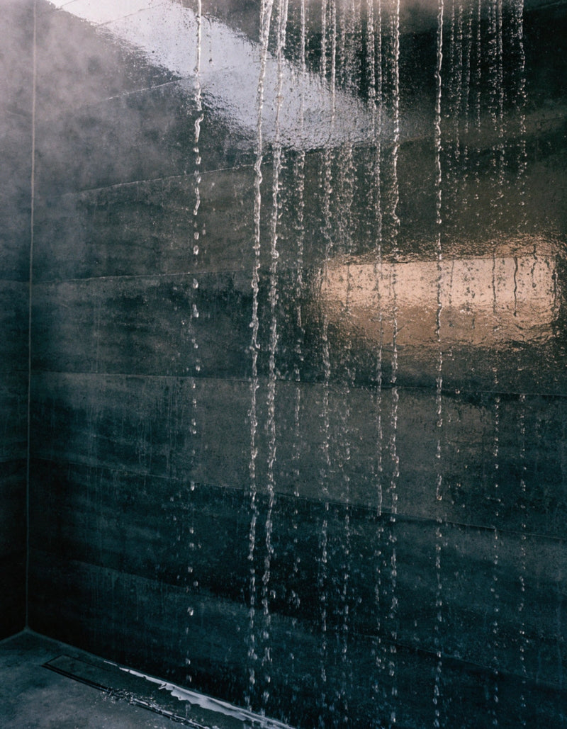 Water streaming down a dark wet stone wall with rising steam and a warm light reflection