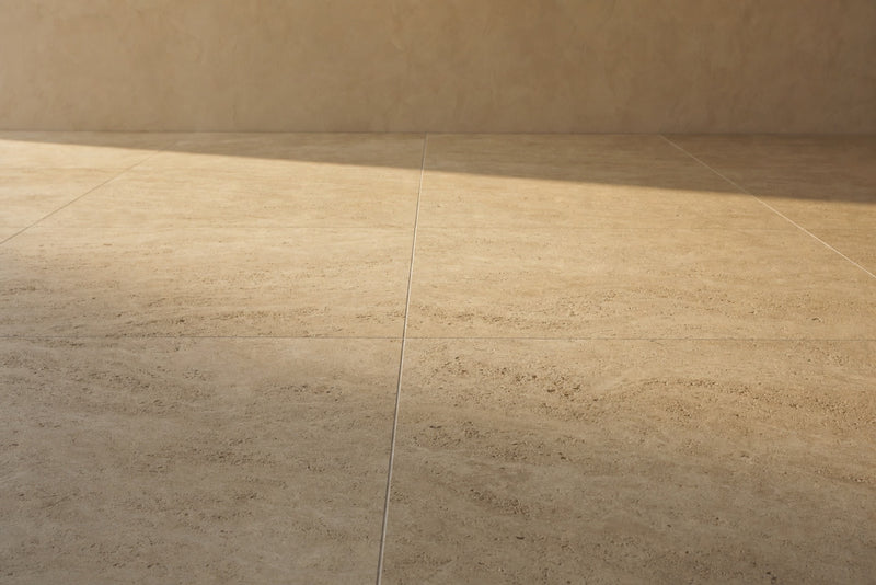Honed pale travertine bathroom floor in warm morning light, the stone grain and veining visible in a quiet empty room