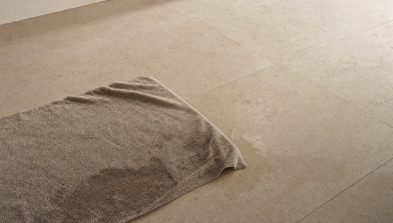 Damp taupe towel lying crumpled on a stone tile floor with wet patches, showing how fabric mats stay soaked