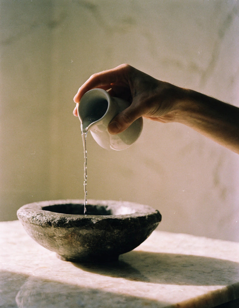 Quiet bathroom — hand pouring water into a stone bowl on marble